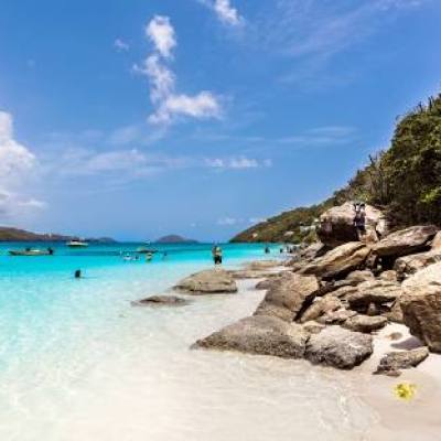 Tropical beach with turquoise water, rocks, and people relaxing under a blue sky with clouds.