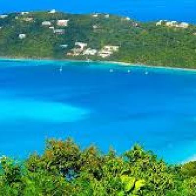 Scenic view of a bay with clear blue water surrounded by green hills and scattered houses.