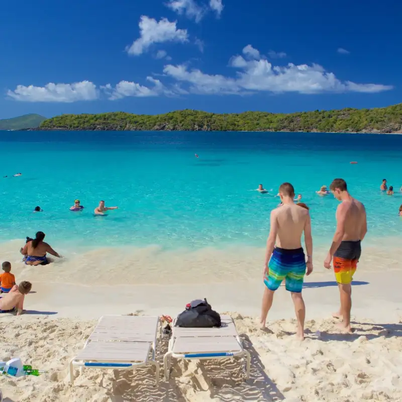 People enjoying a sunny day at a tropical beach with clear blue water and white sand.