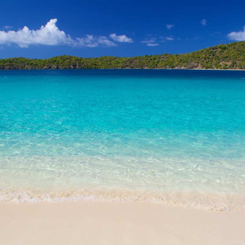 Tropical beach with clear turquoise water, distant islands, and blue sky.