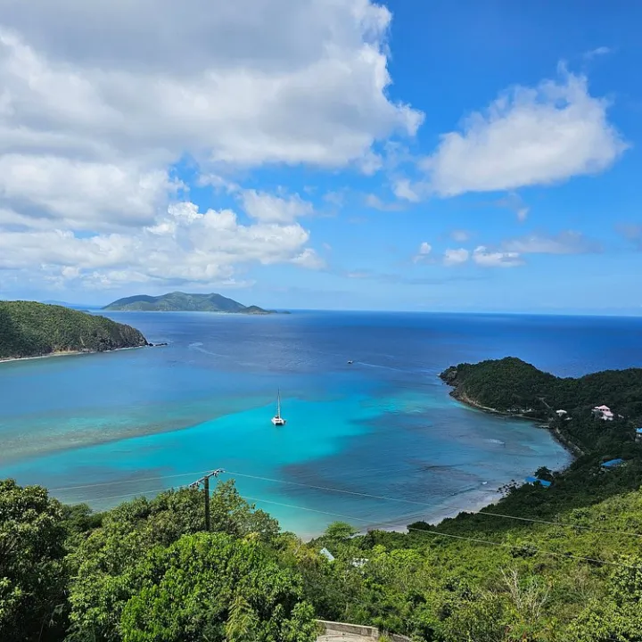Scenic view of a tropical bay with turquoise waters and sailboats, surrounded by lush green hills.