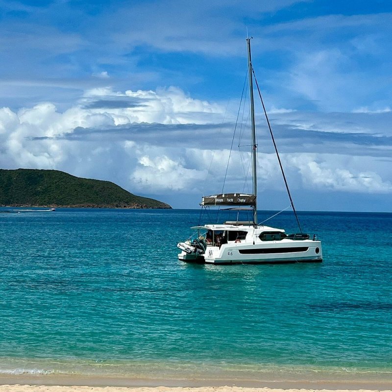 Sailboat anchored in clear turquoise sea near a sandy beach under a blue sky.