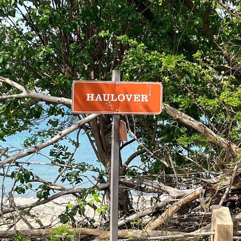 Red sign with 'Haulover' in white, near trees and a beach in the background.