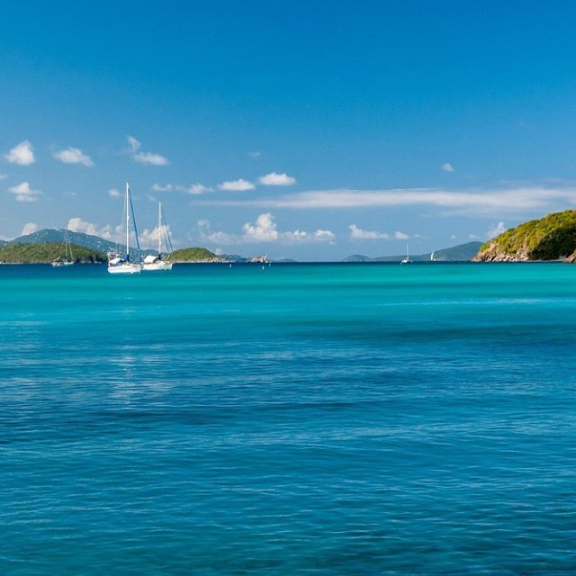 Sailboats on turquoise sea with islands and a clear blue sky.