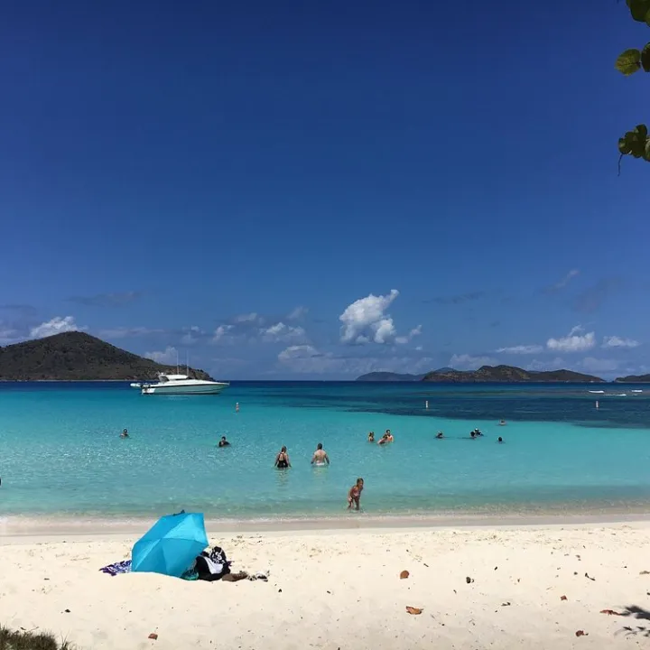 Beach scene with people swimming, a boat, and an umbrella on the sand.