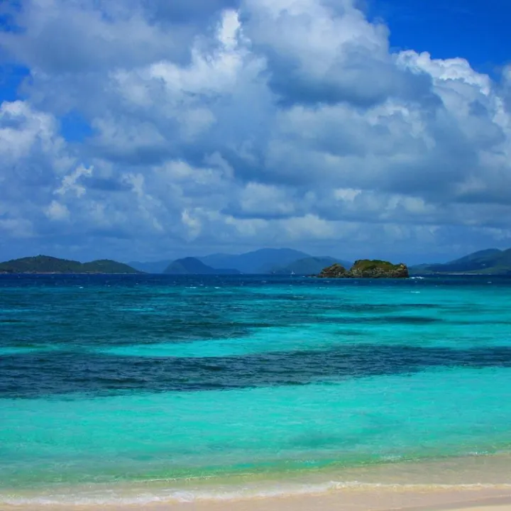 Tropical beach with turquoise ocean, small island, and cloudy sky.
