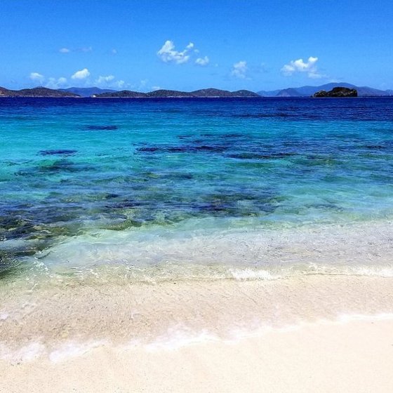 Tropical beach with clear turquoise water and distant islands under a blue sky.