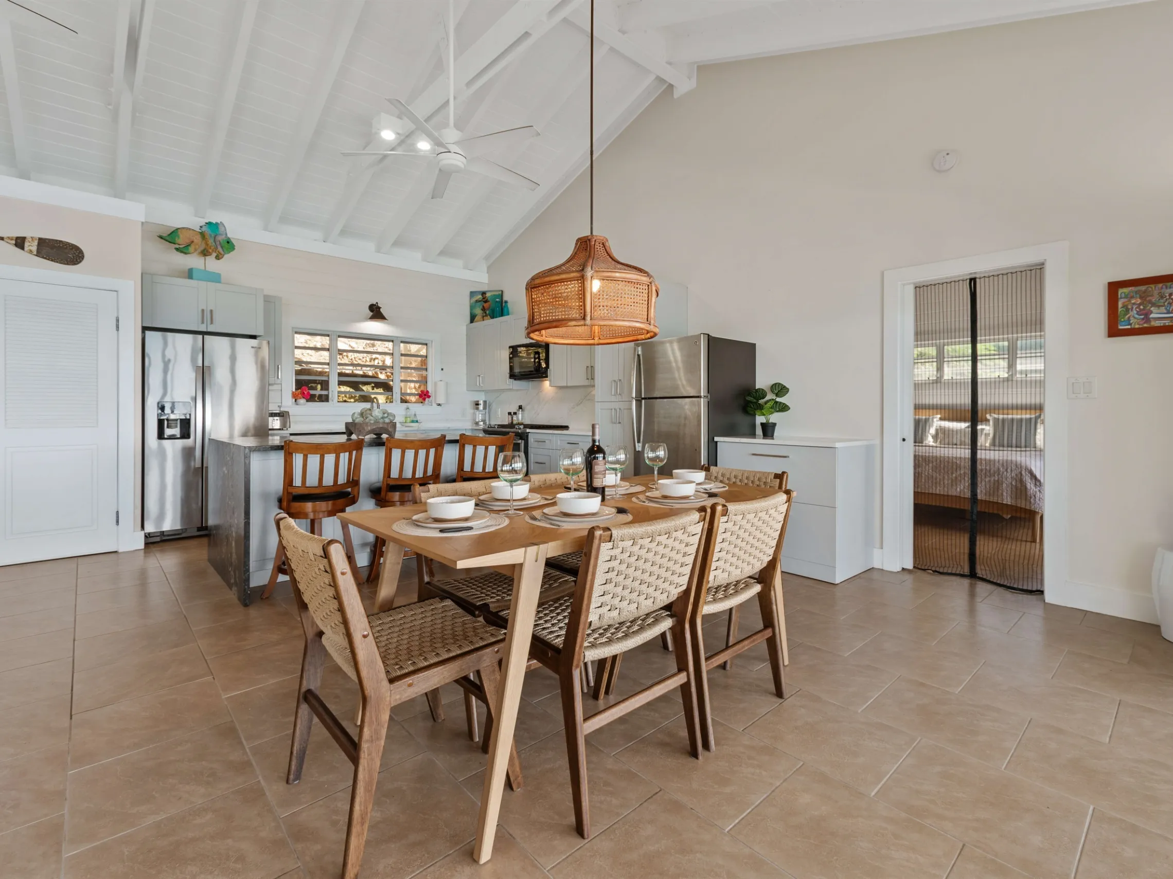 Open kitchen and dining area with a table set for six, wicker chairs, and visible bedroom doorway.