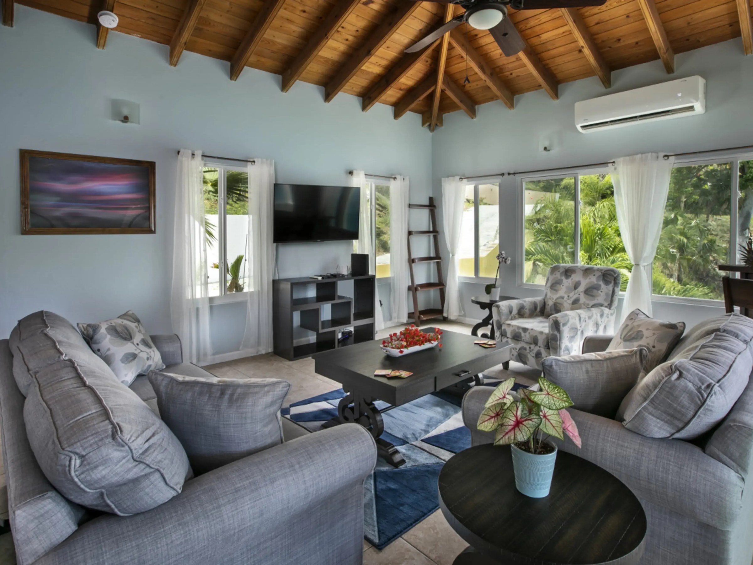 Cozy living room with gray sofas, floral chairs, and a wooden ceiling.