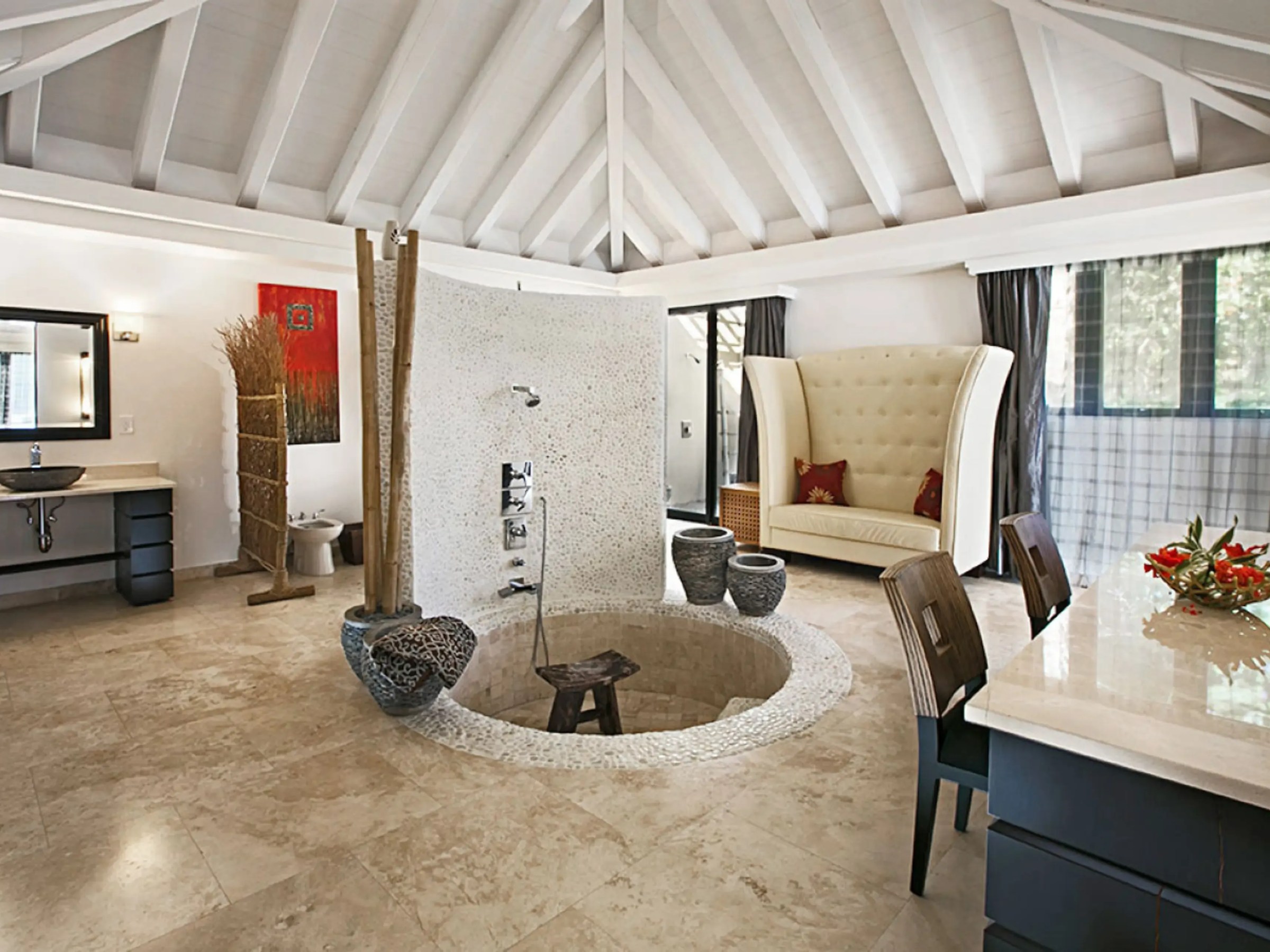 Spacious bathroom with sunken shower, modern decor, large chair, and countertop with flowers.