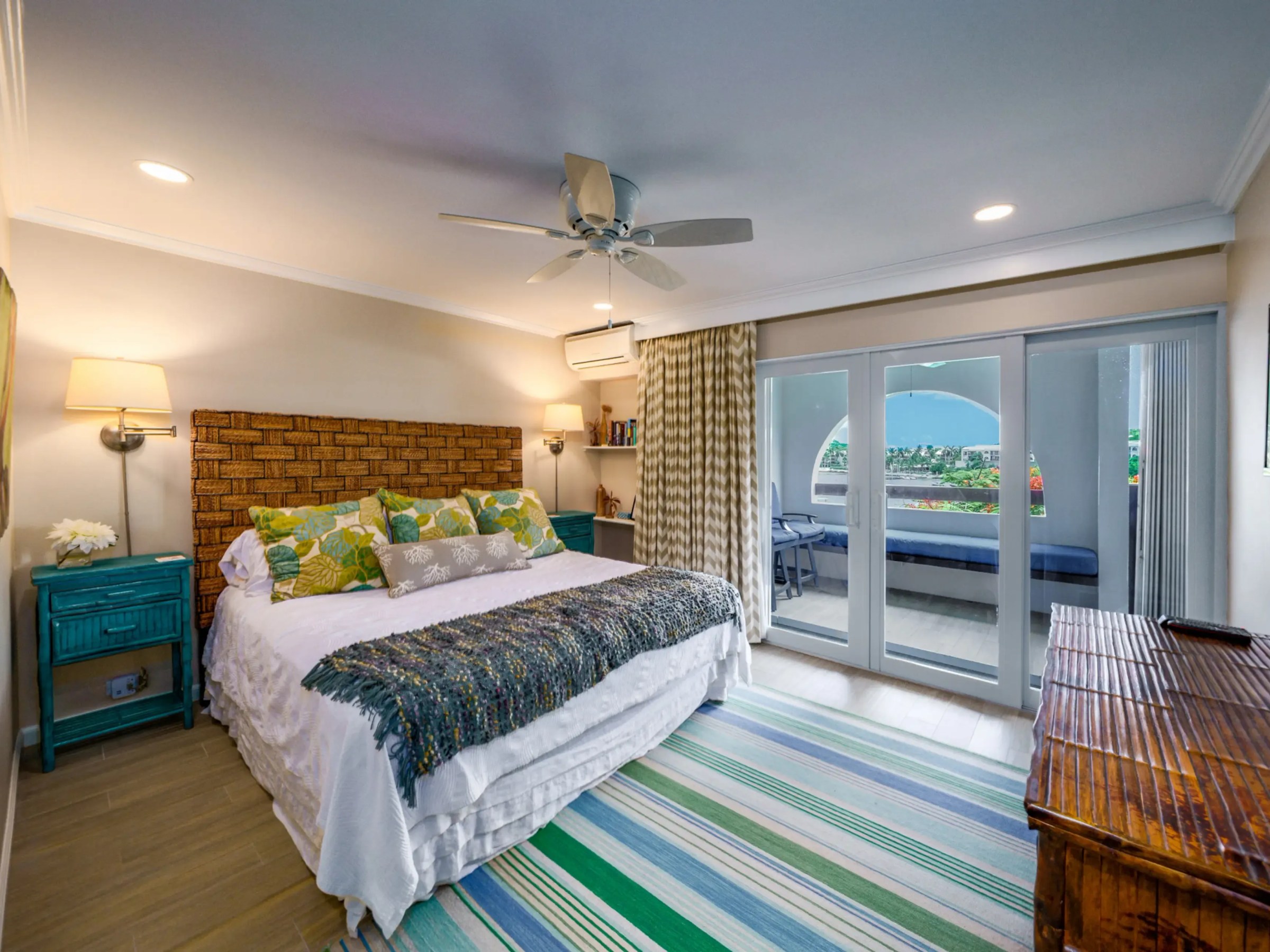 Bright bedroom with king bed, colorful pillows, balcony view, and cozy decor.