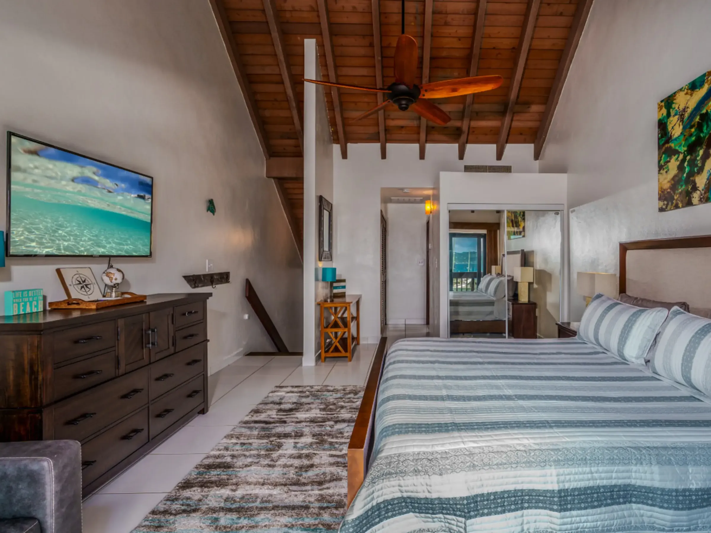 Cozy bedroom with wooden ceiling, striped bed, dresser, TV, and modern decor.