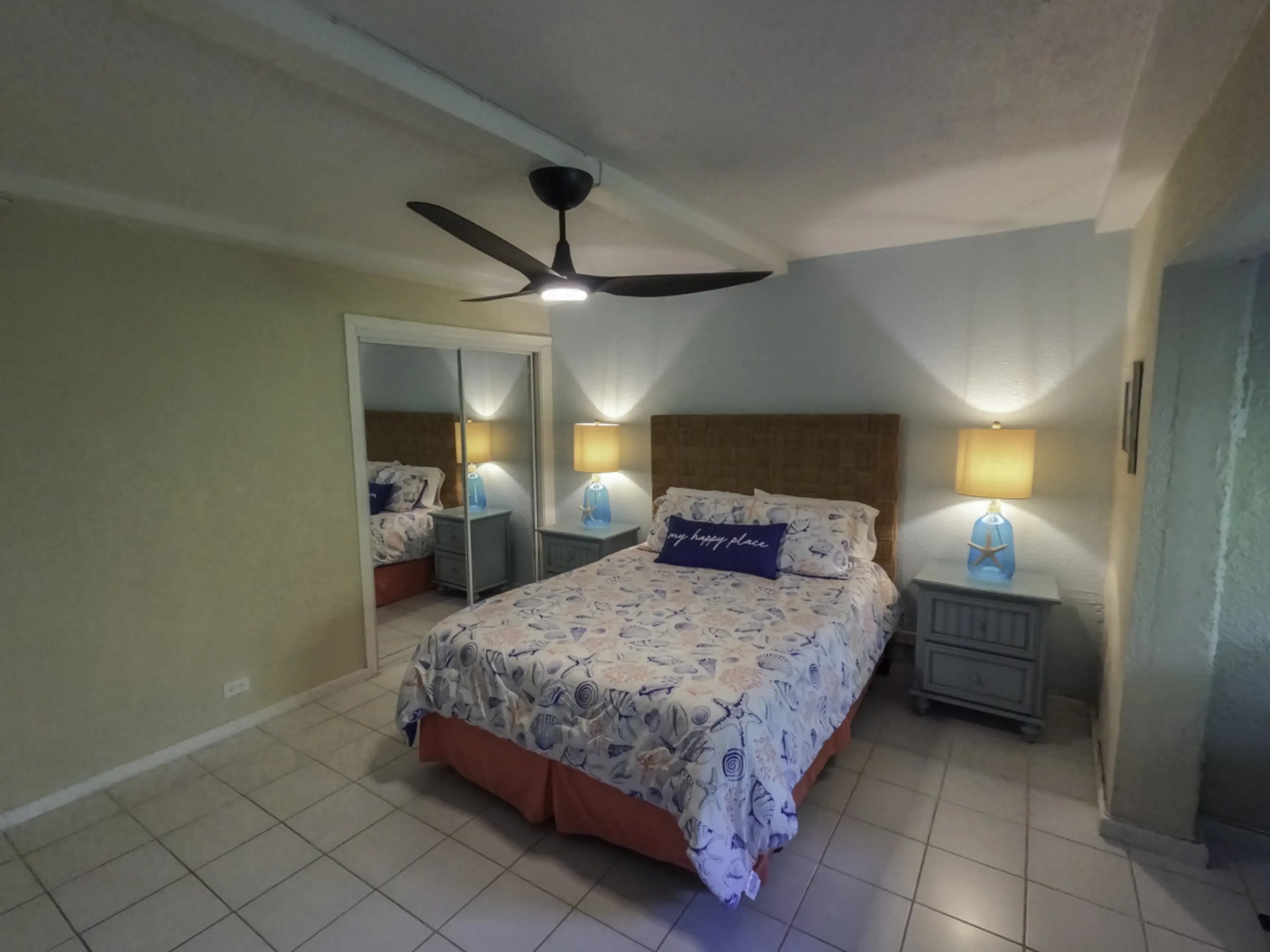 Cozy bedroom with floral bedspread, mirrored closet, ceiling fan, and bedside lamps.