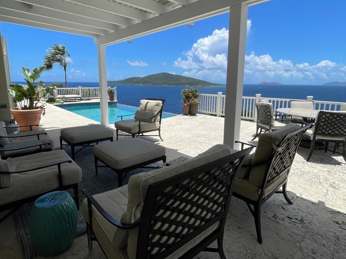 Patio with chairs and table overlooking ocean and island, near pool.