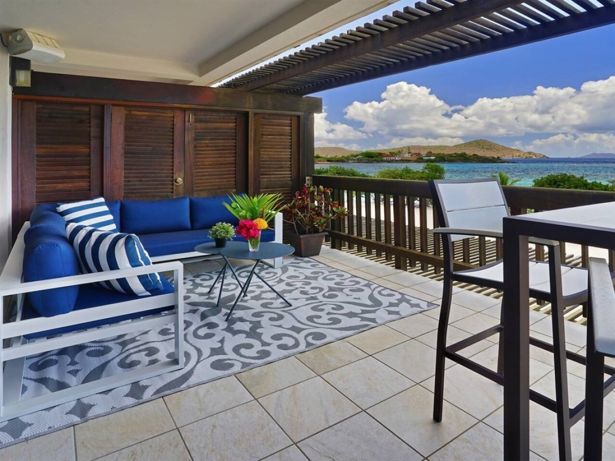 Outdoor patio with blue sofa, table, high chairs, and ocean view.