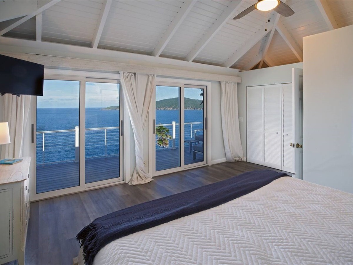 Bedroom with ocean view, wood ceiling, sliding glass doors, and a ceiling fan.