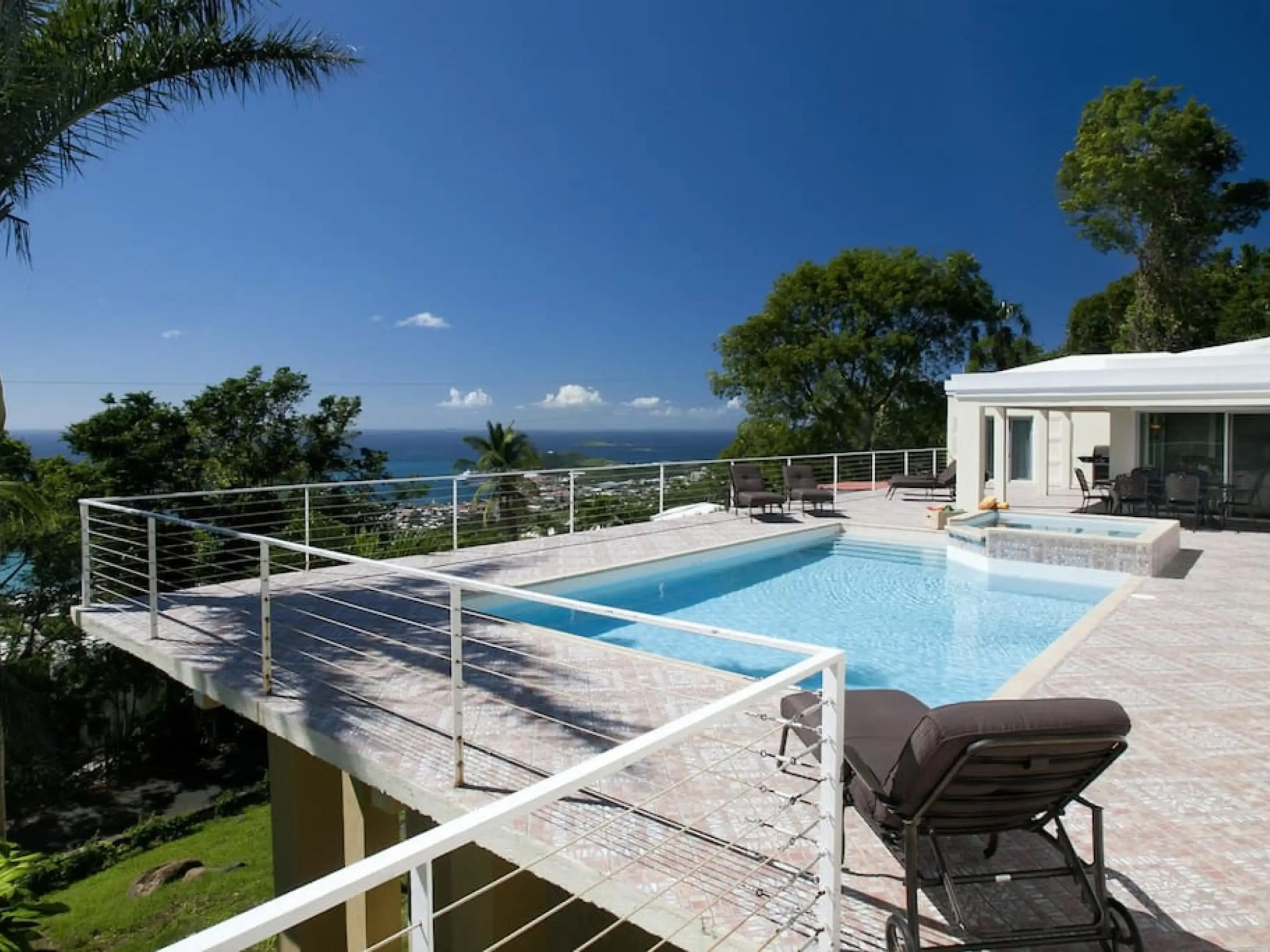 Modern patio with pool, lounge chairs, ocean view, and surrounded by trees.