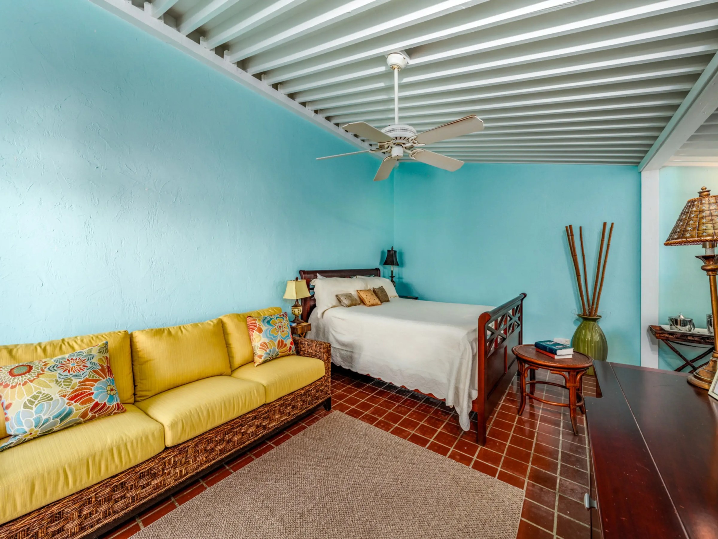 Room with blue walls, bed, yellow sofa, ceiling fan, and wooden furniture.
