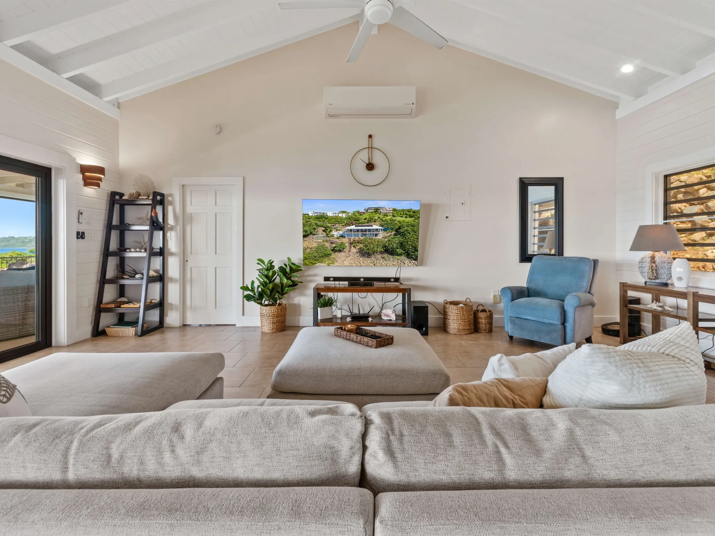 Modern living room with a TV, large sofa, armchair, and a view of the outdoors through sliding glass doors.