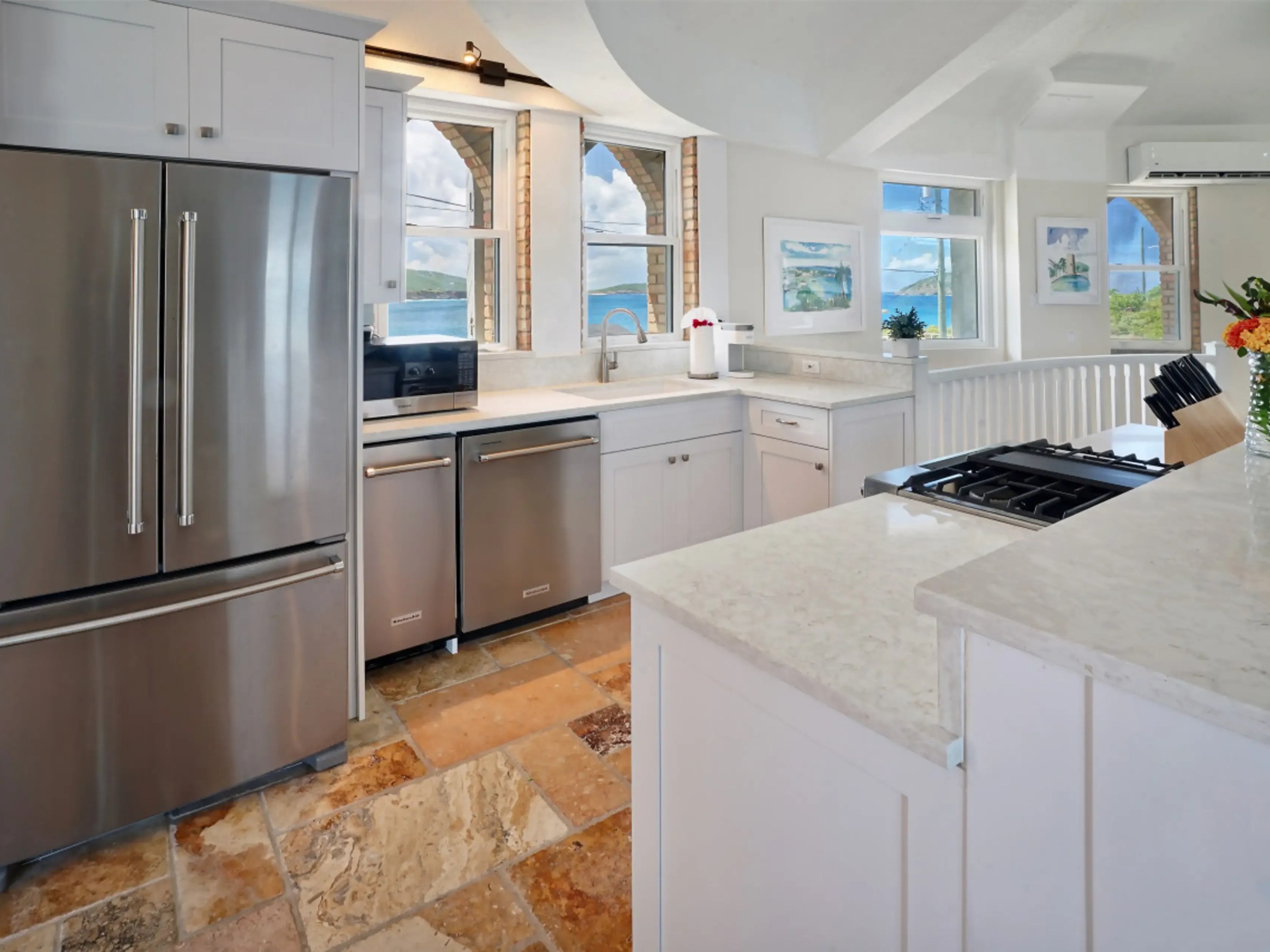 Modern kitchen with stainless steel appliances, white cabinets, and large windows overlooking the ocean.