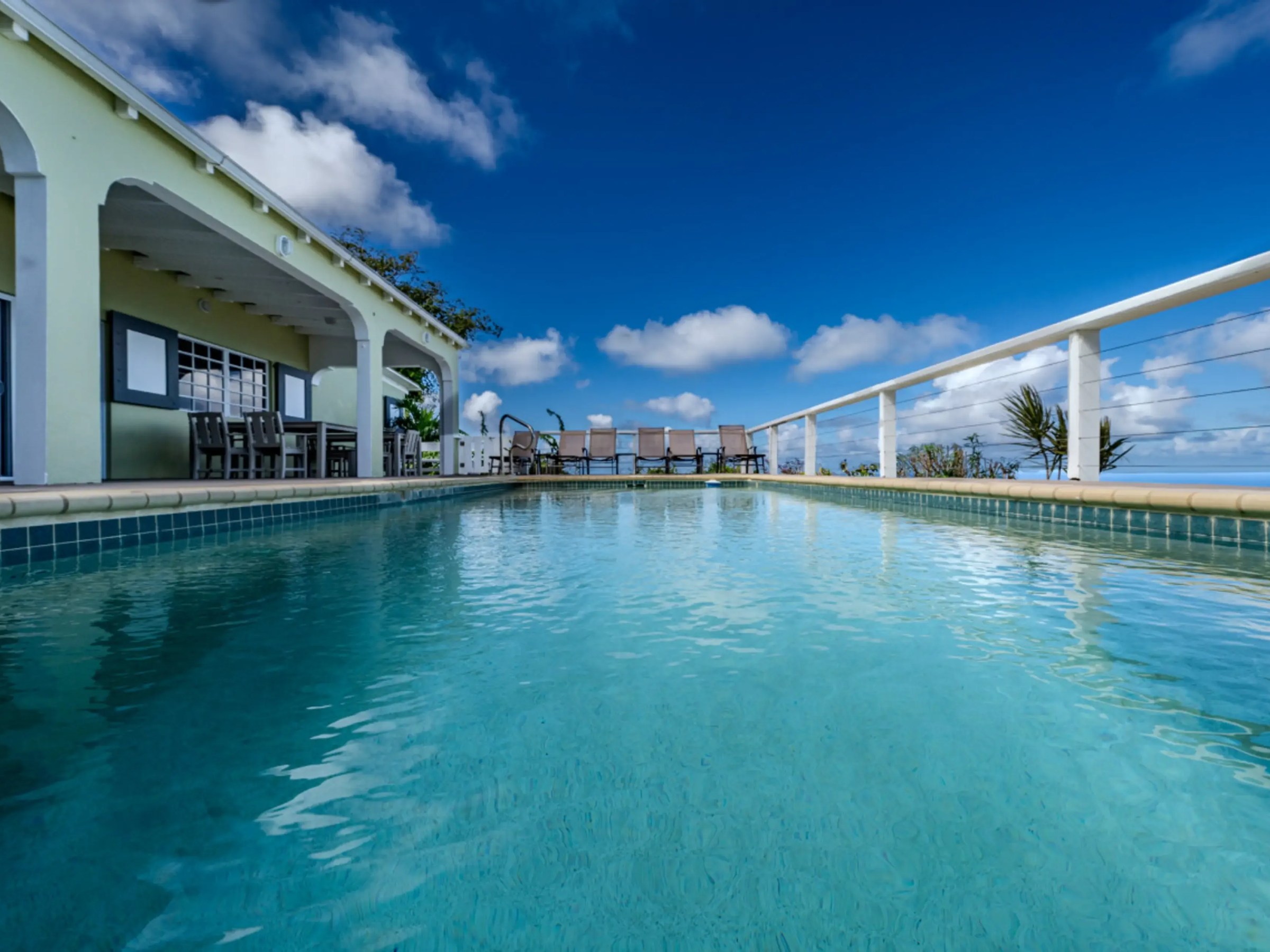 Swimming pool with patio view, loungers, and ocean under clear blue sky.