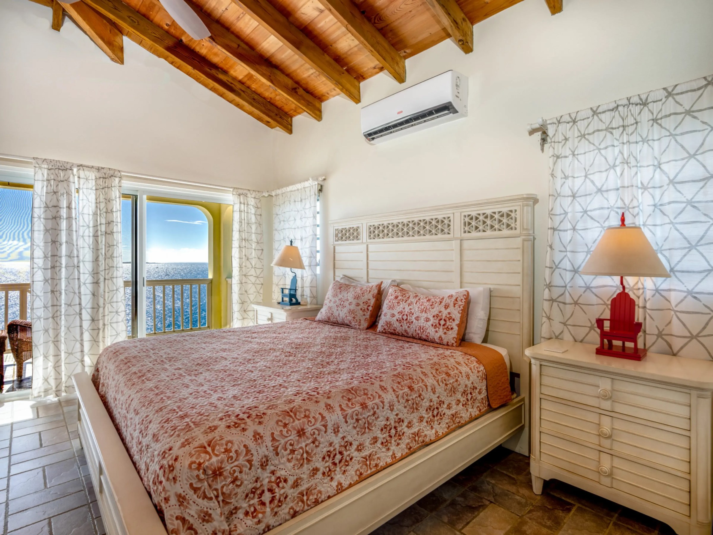 Bedroom with wooden ceiling, ocean view, king bed, patterned bedding, and two bedside tables with lamps.