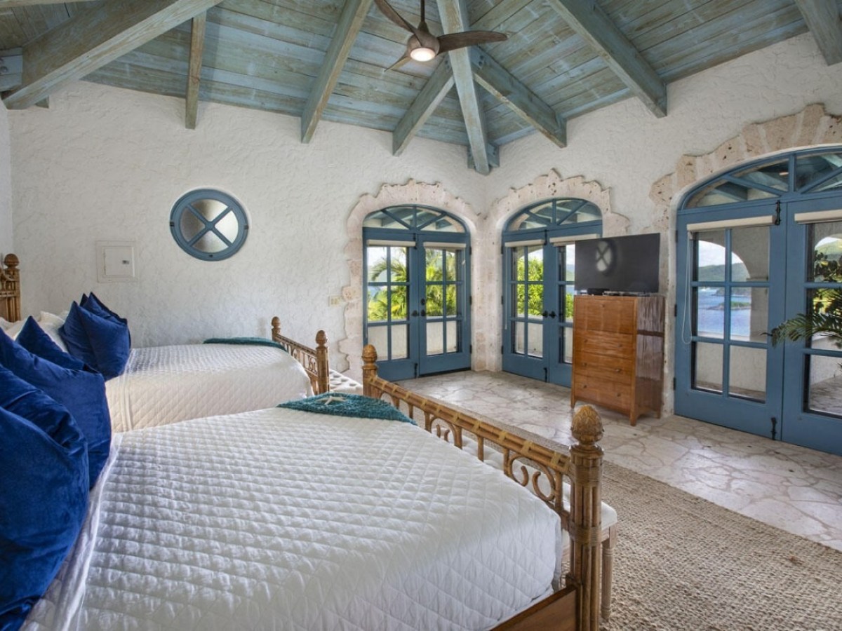 Cozy bedroom with two beds, blue accents, and large windows overlooking greenery.