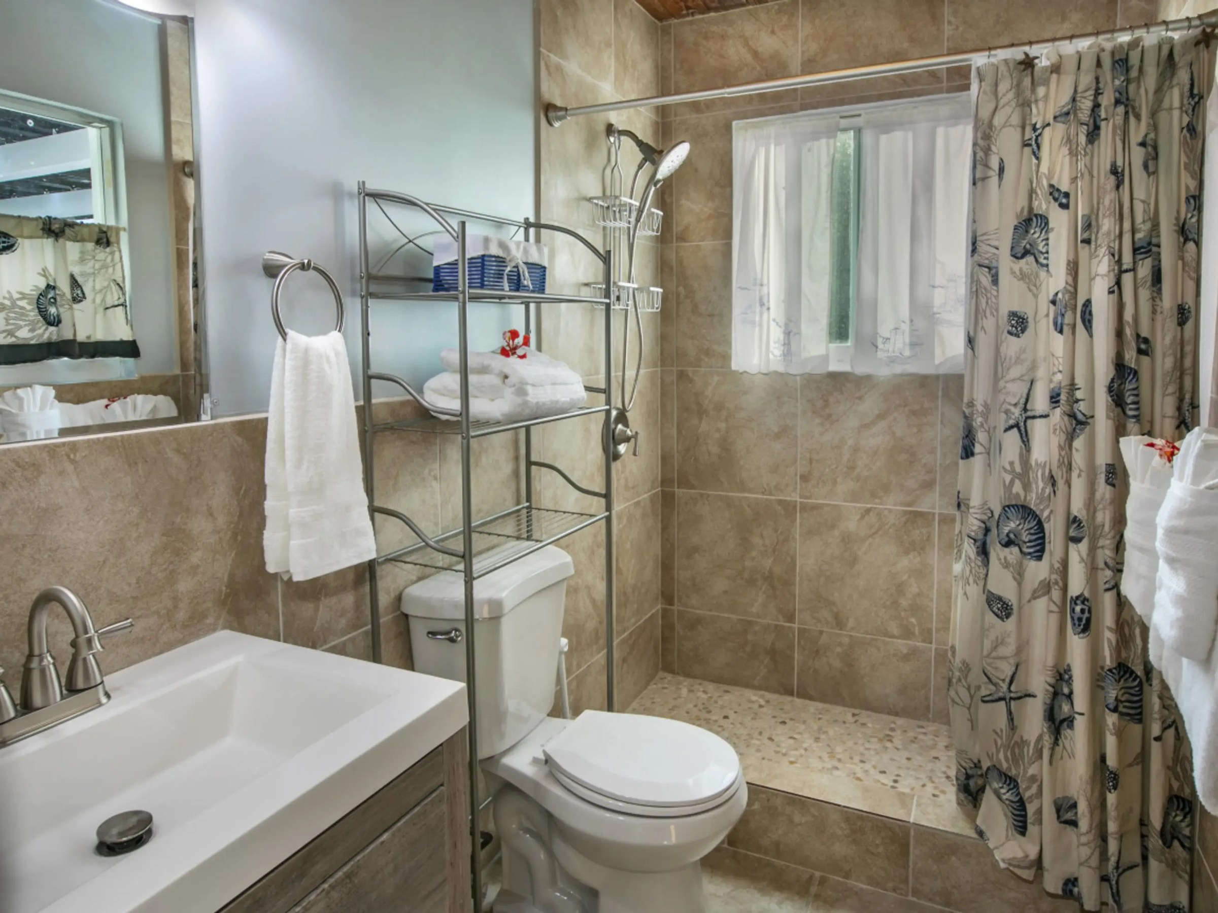 Modern bathroom with tiled shower, sink, toilet, and metal shelving with towels.