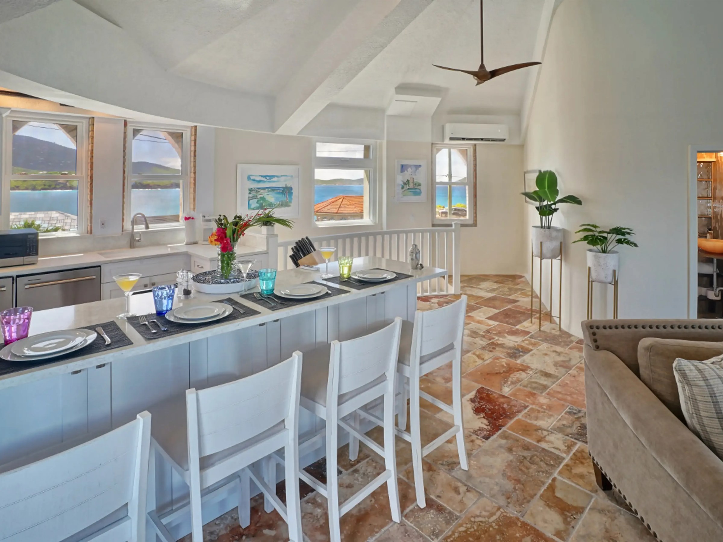 Open kitchen with bar seating, white decor, large windows, and a distant ocean view.