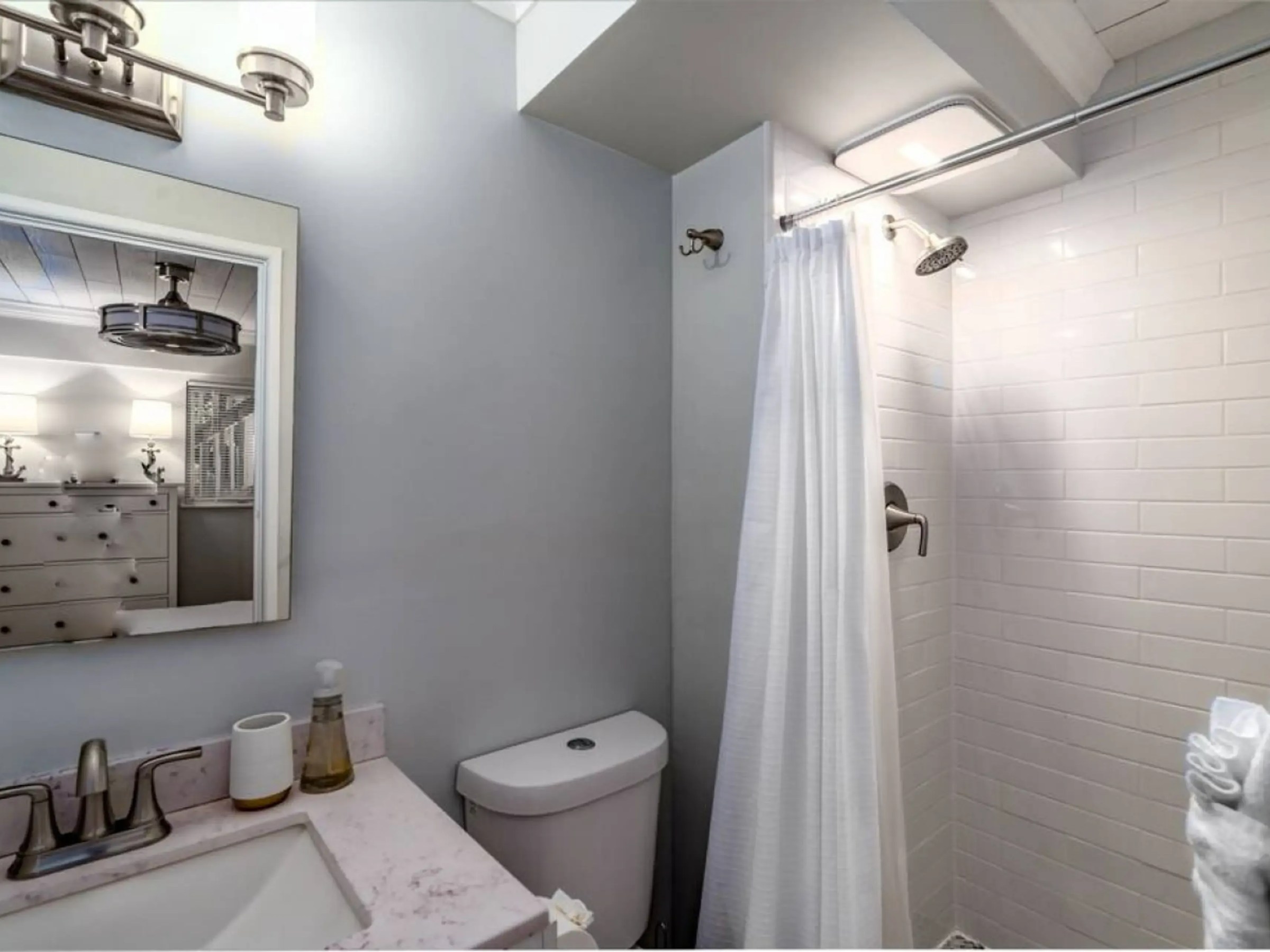 Bathroom with a sink, toilet, mirror, shower curtain, and tiled walls.