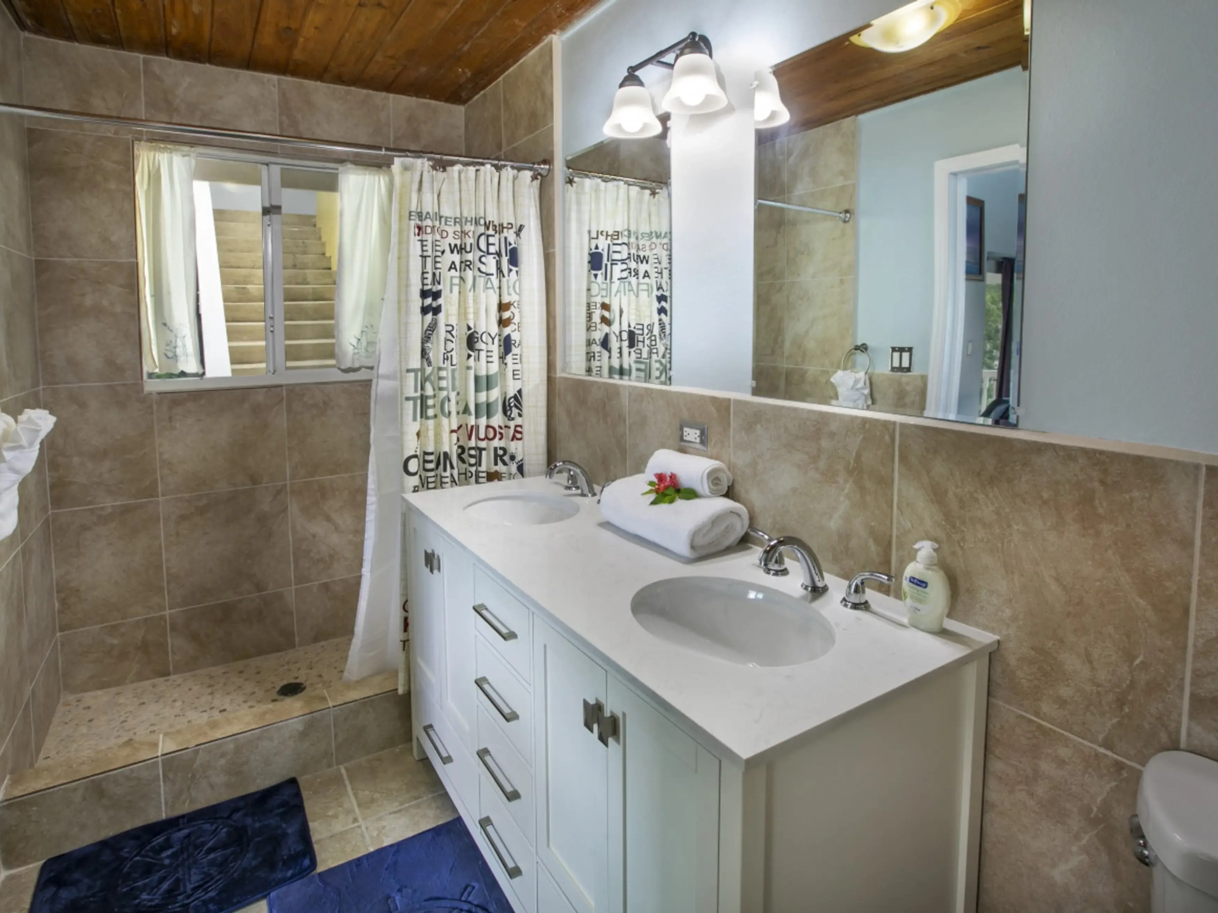 Bathroom with double sinks, large mirror, towel rack, and shower with patterned curtain.