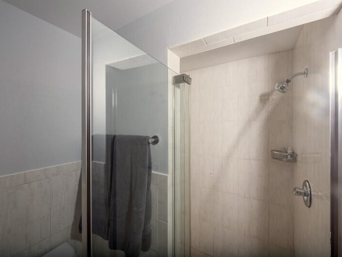 Glass-enclosed shower with gray towel hanging, showerhead spraying water