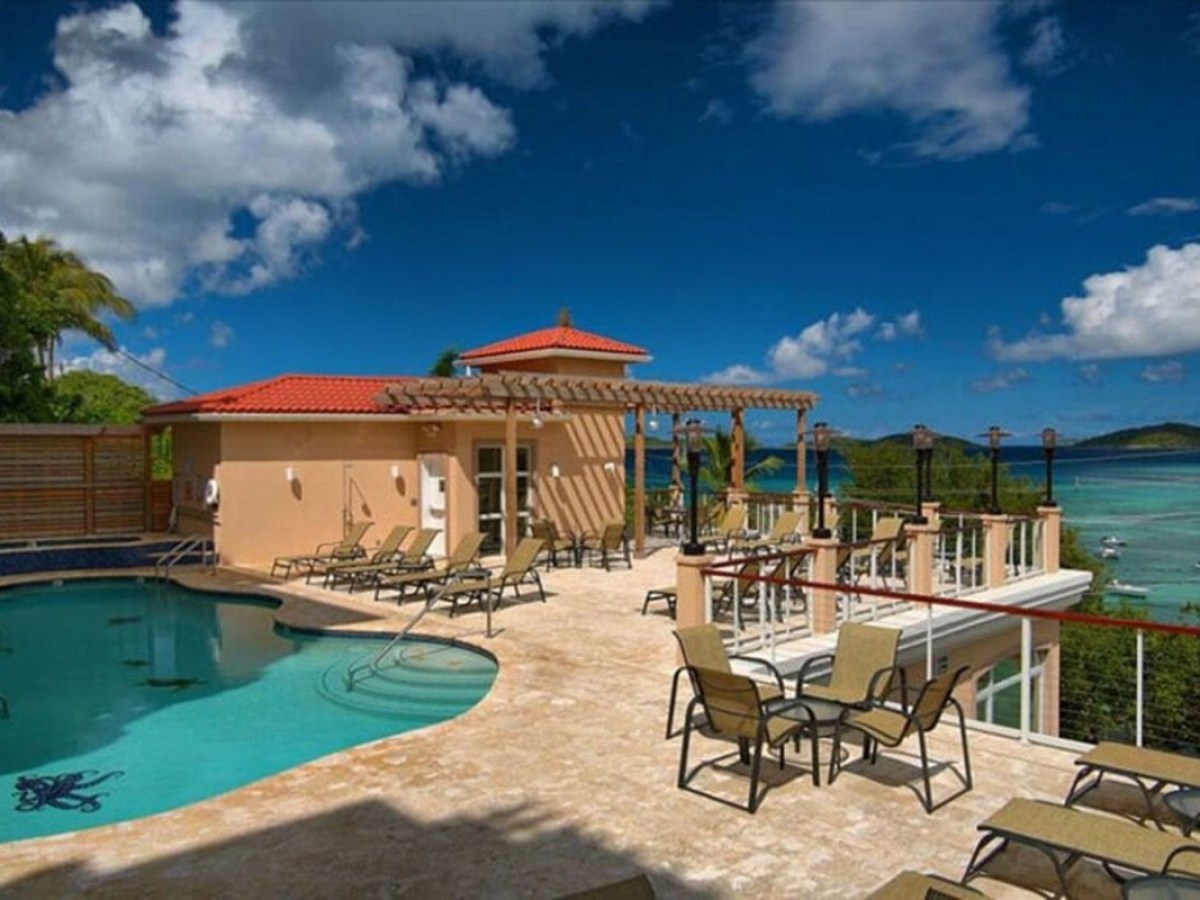 Outdoor pool area with lounge chairs overlooking a tropical beach and ocean.