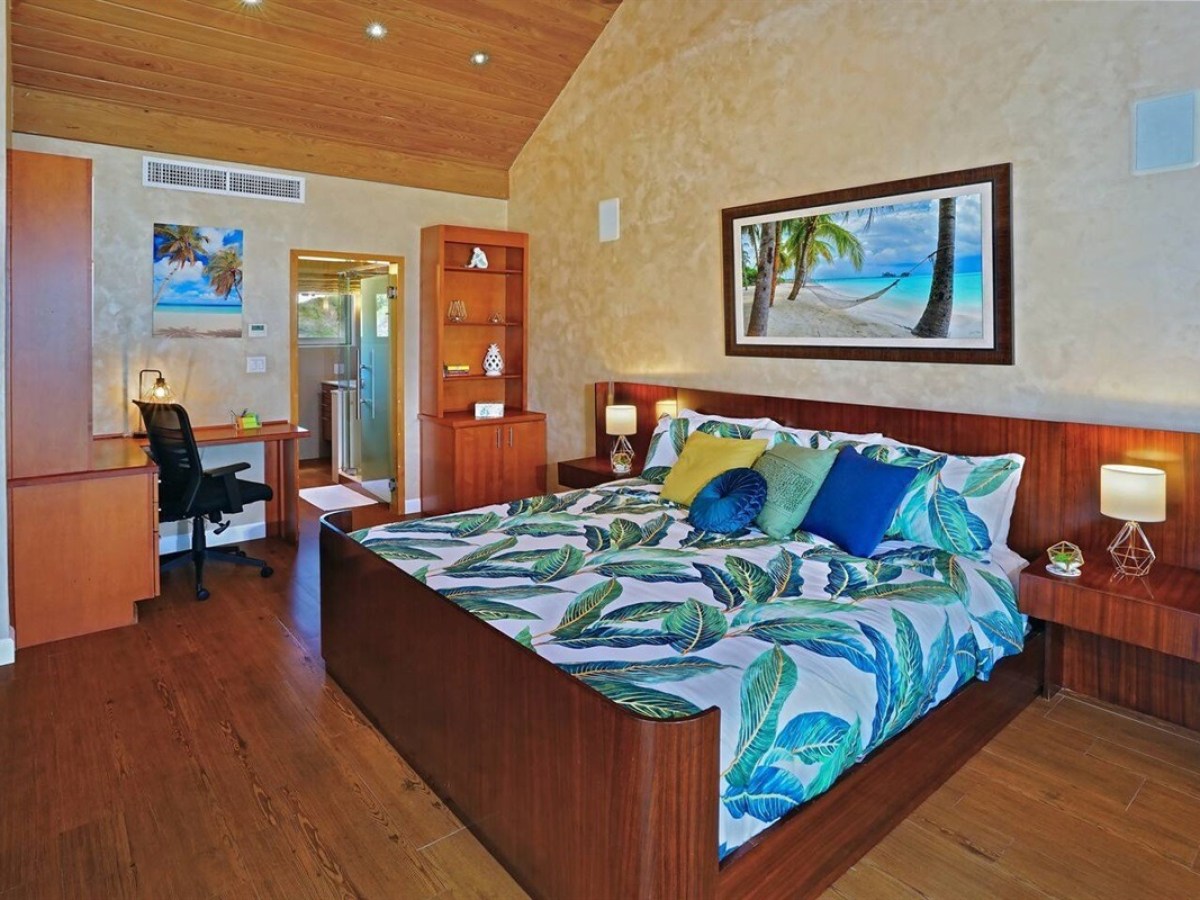 Tropical-themed bedroom with leaf-patterned bedding, wooden furniture, and beach artwork on the wall.