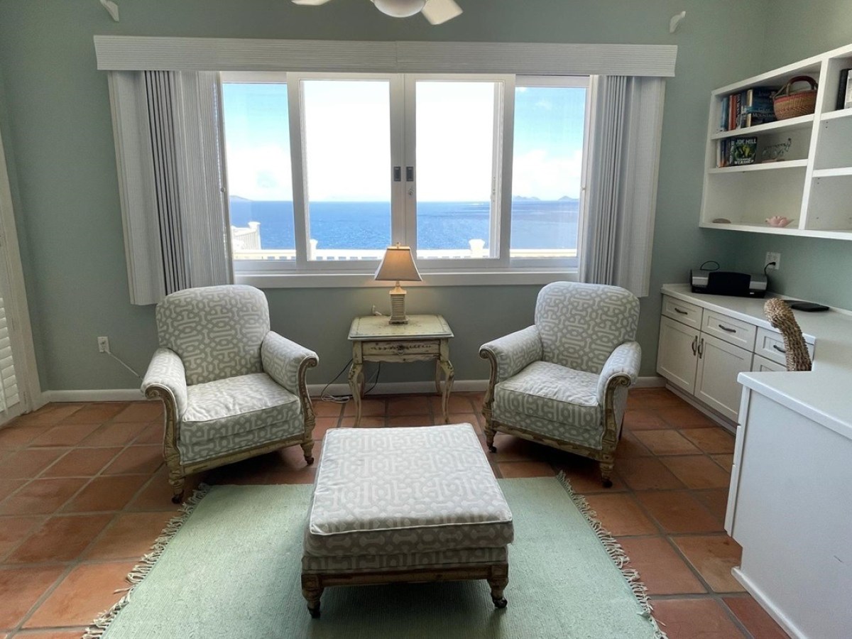 Cozy room with two armchairs, an ottoman, a small table, and a window showing an ocean view.
