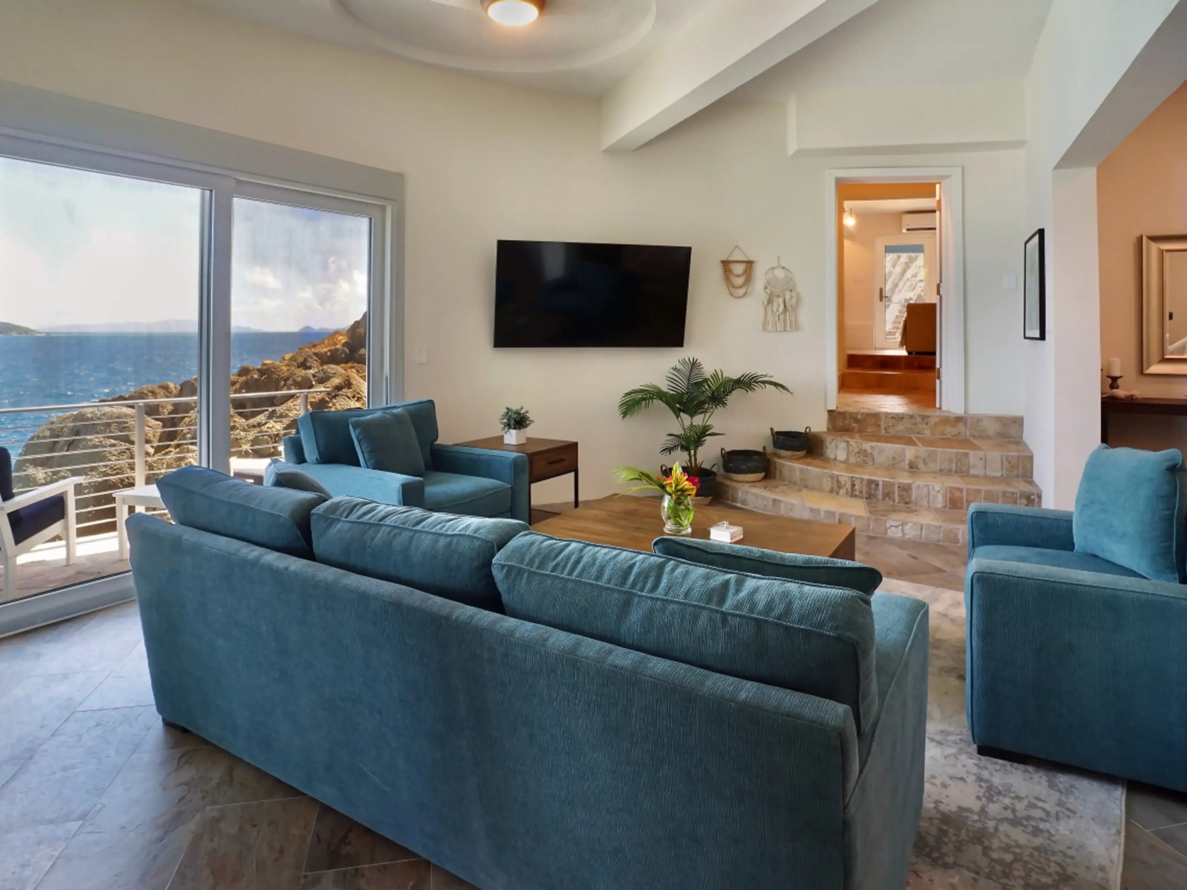 Living room with blue sofas, TV, large window with ocean view, and stairs to another room.