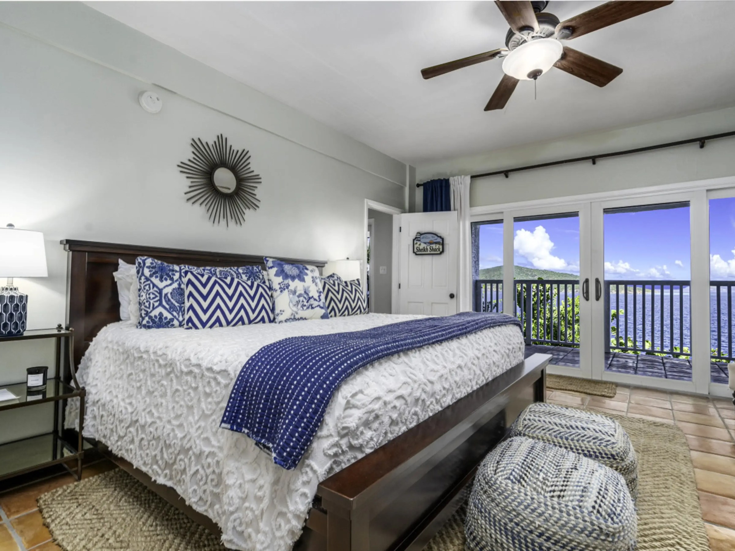 Cozy bedroom with blue accents, ocean view, and glass doors leading to a balcony.