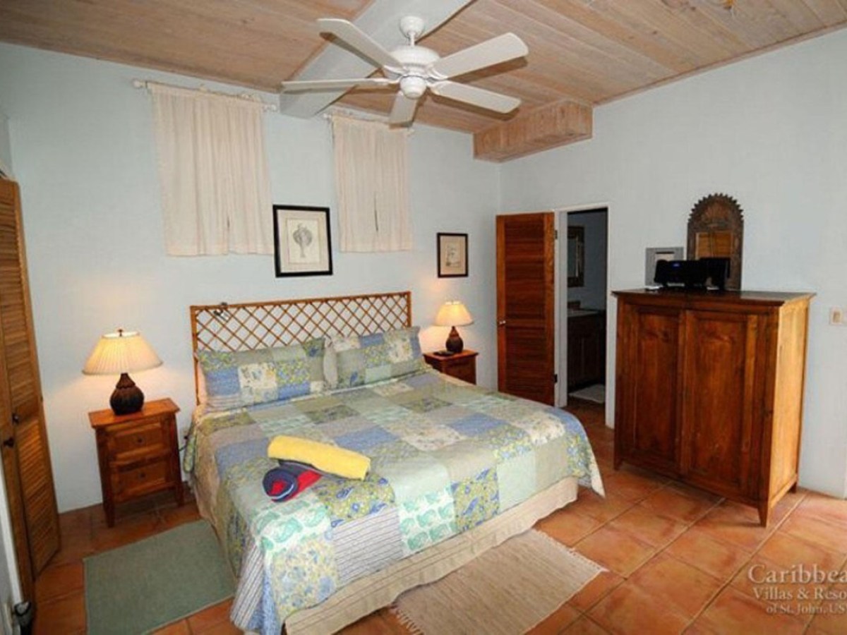Bedroom with a wooden bed, patchwork quilt, ceiling fan, nightstands, and an armoire in warm tones.