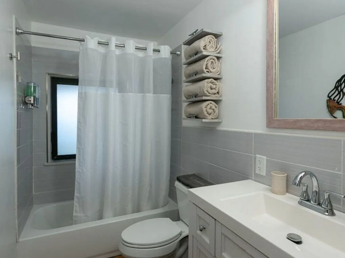 Modern bathroom with shower, white curtain, vanity, towel rack, and large mirror.