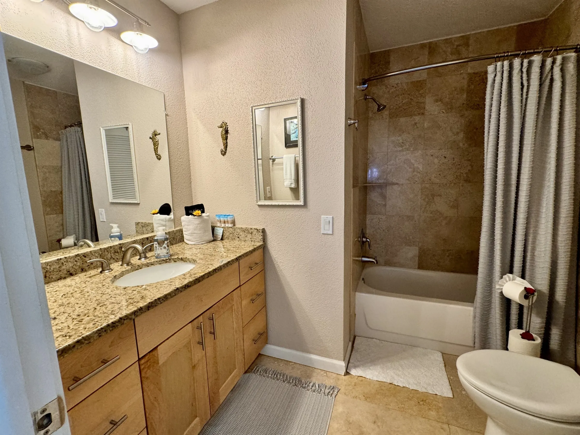 Bathroom with granite countertop, double sink, bathtub, and beige tiles.