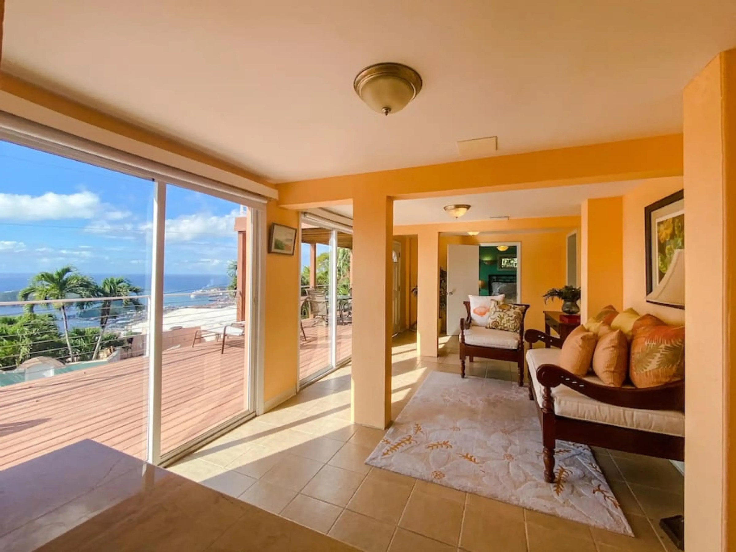 Bright room with ocean view, beige tiles, orange walls, chairs with cushions, and glass sliding doors.
