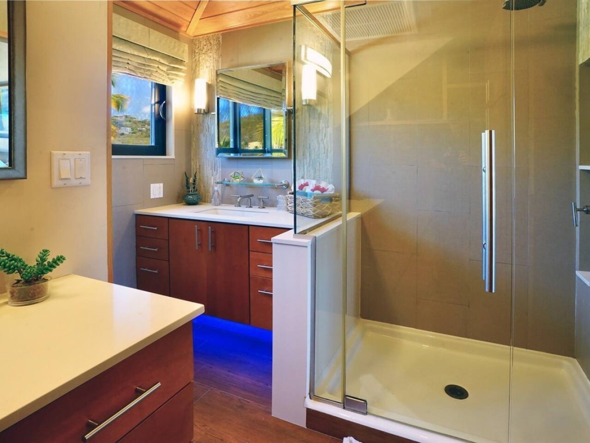 Modern bathroom with glass shower, wooden cabinets, and blue ambient lighting.