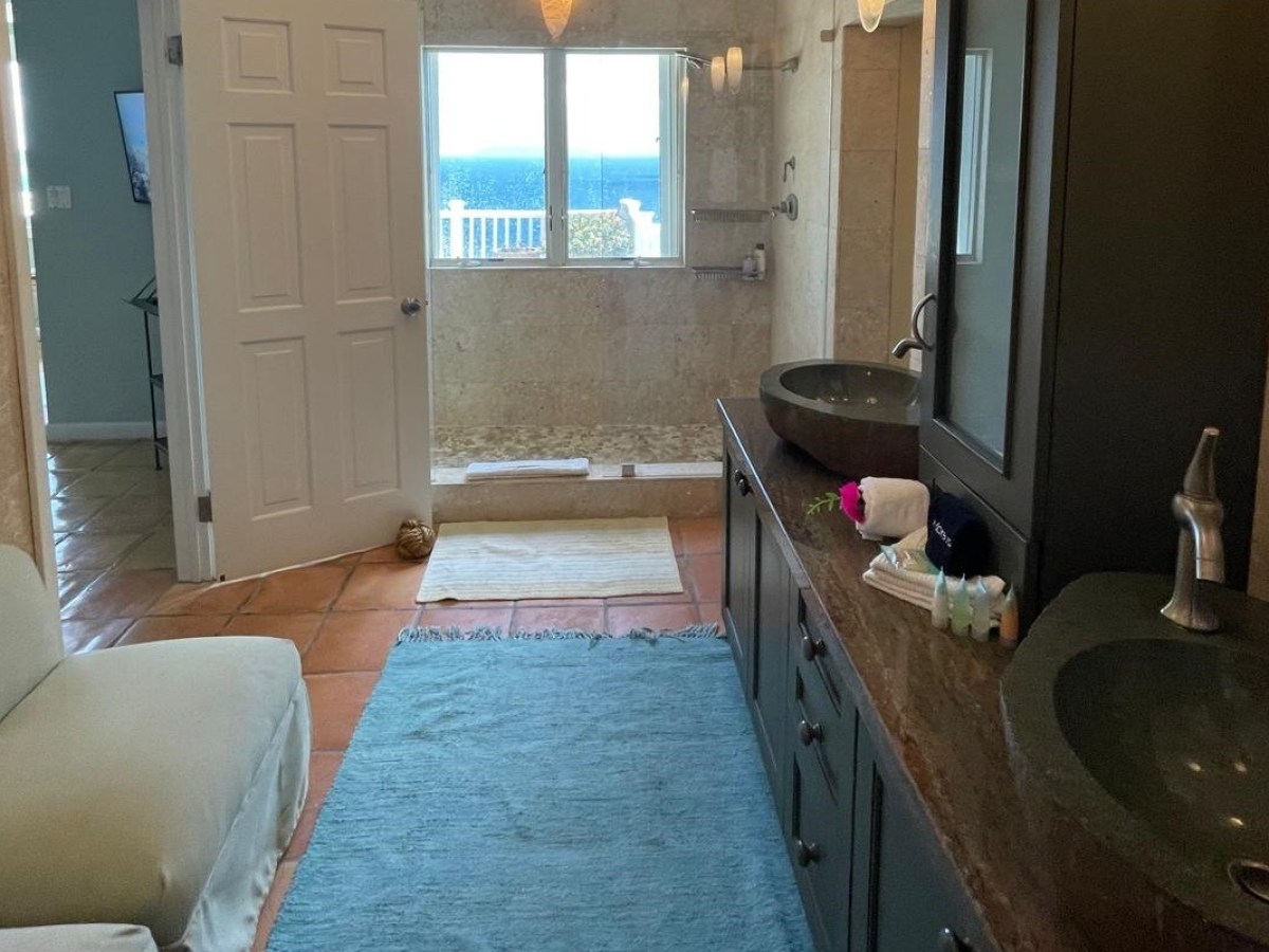 Bathroom with double sink, blue rug, and ocean view through window.