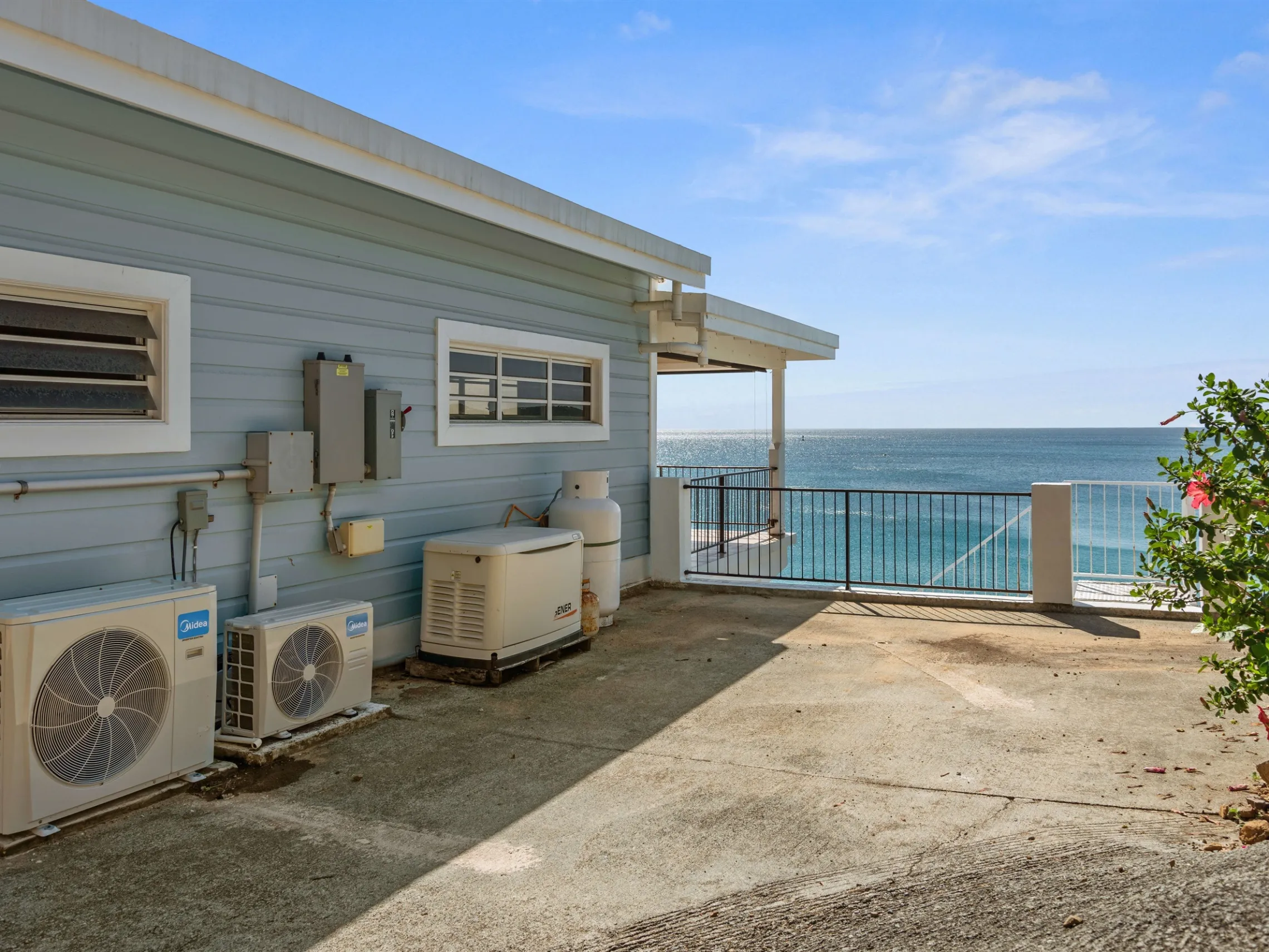 House exterior with AC units, ocean view, and a hibiscus bush by the patio.