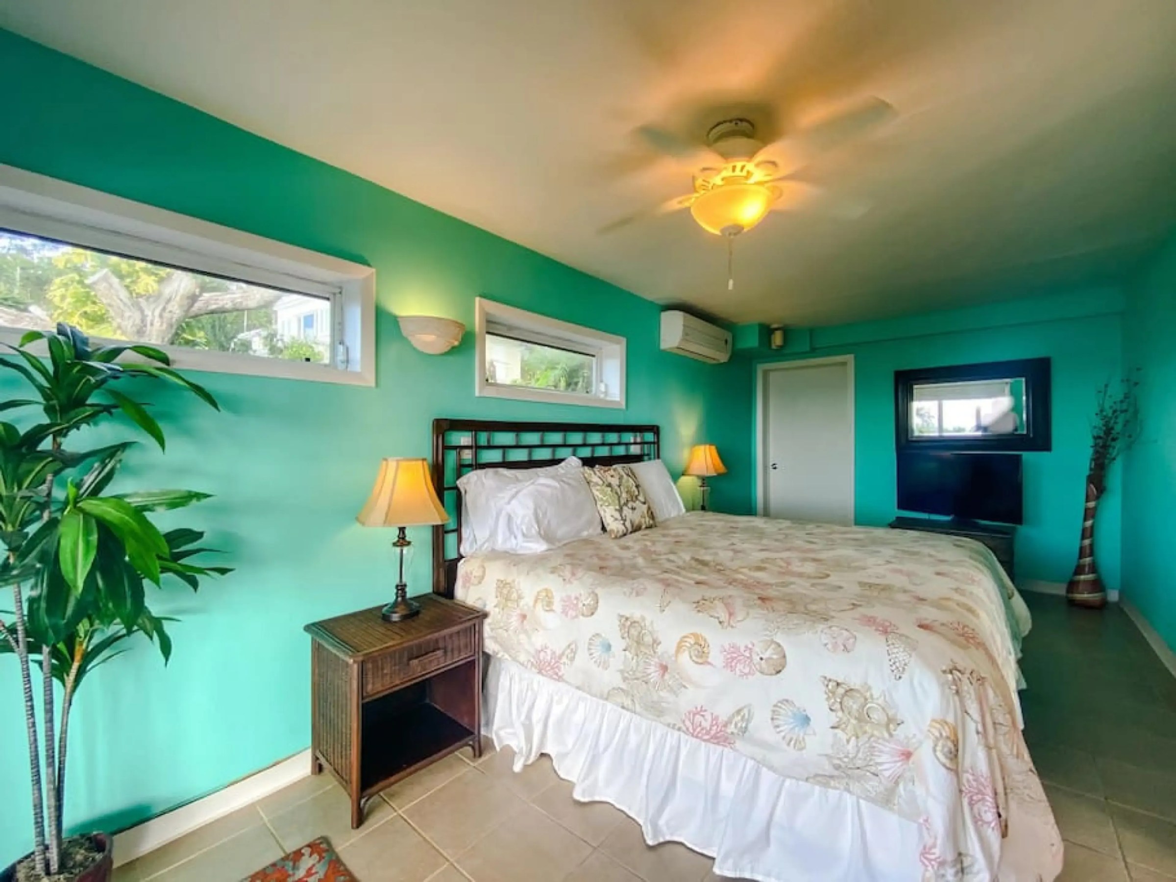 Bright bedroom with turquoise walls, large bed, bedside lamp, and plants.