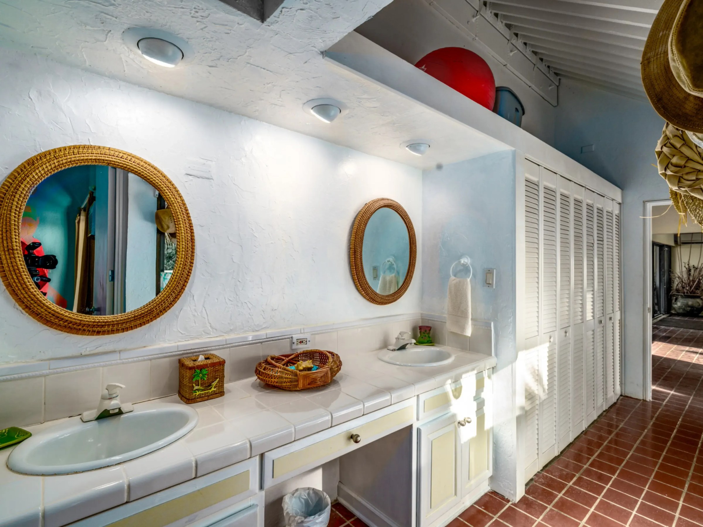 Bright bathroom with two circular mirrors, white sinks, and wicker baskets on tiled counter.