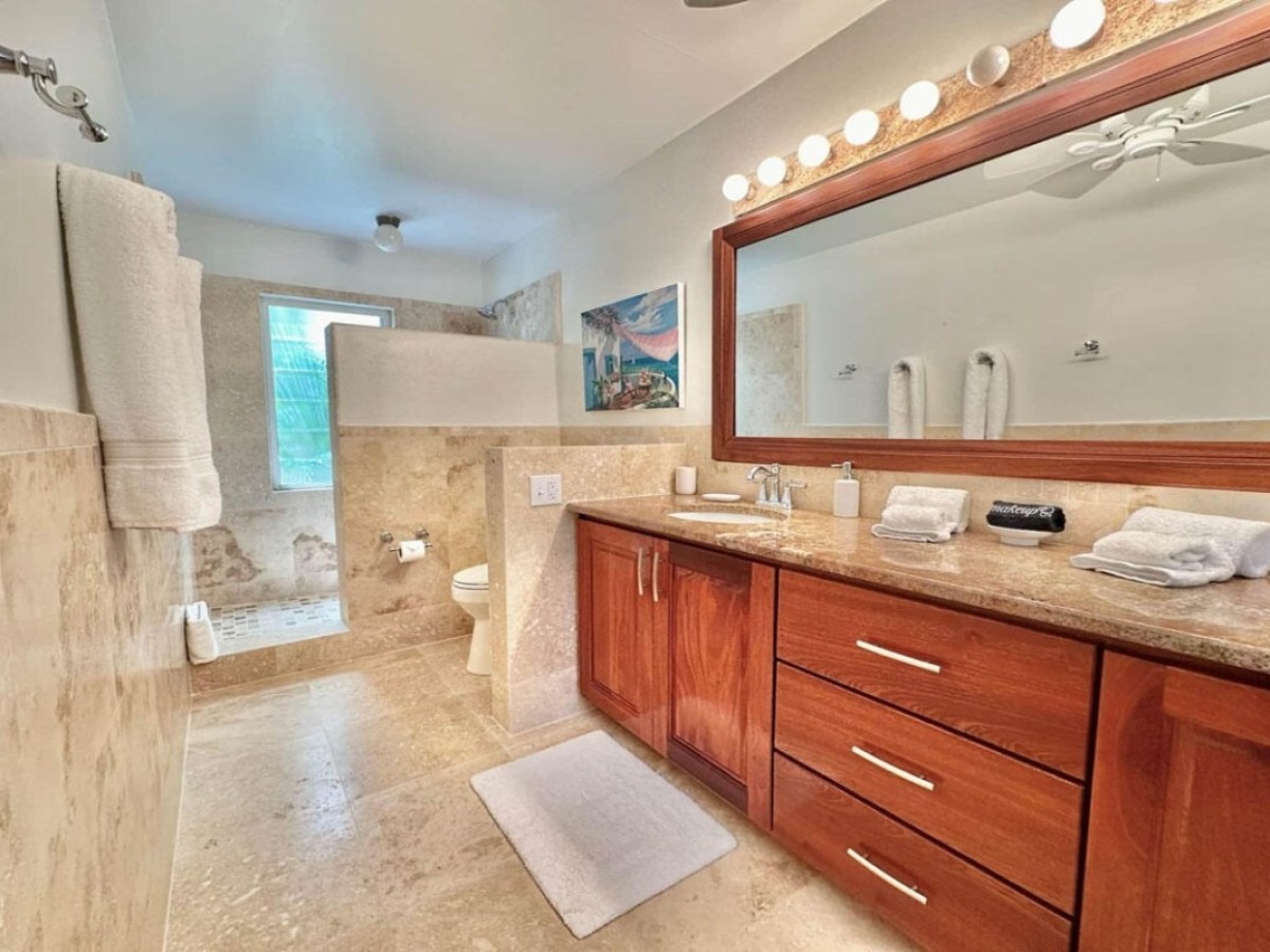 Modern bathroom with wooden vanity, large mirror, tiled shower, and towels on racks.