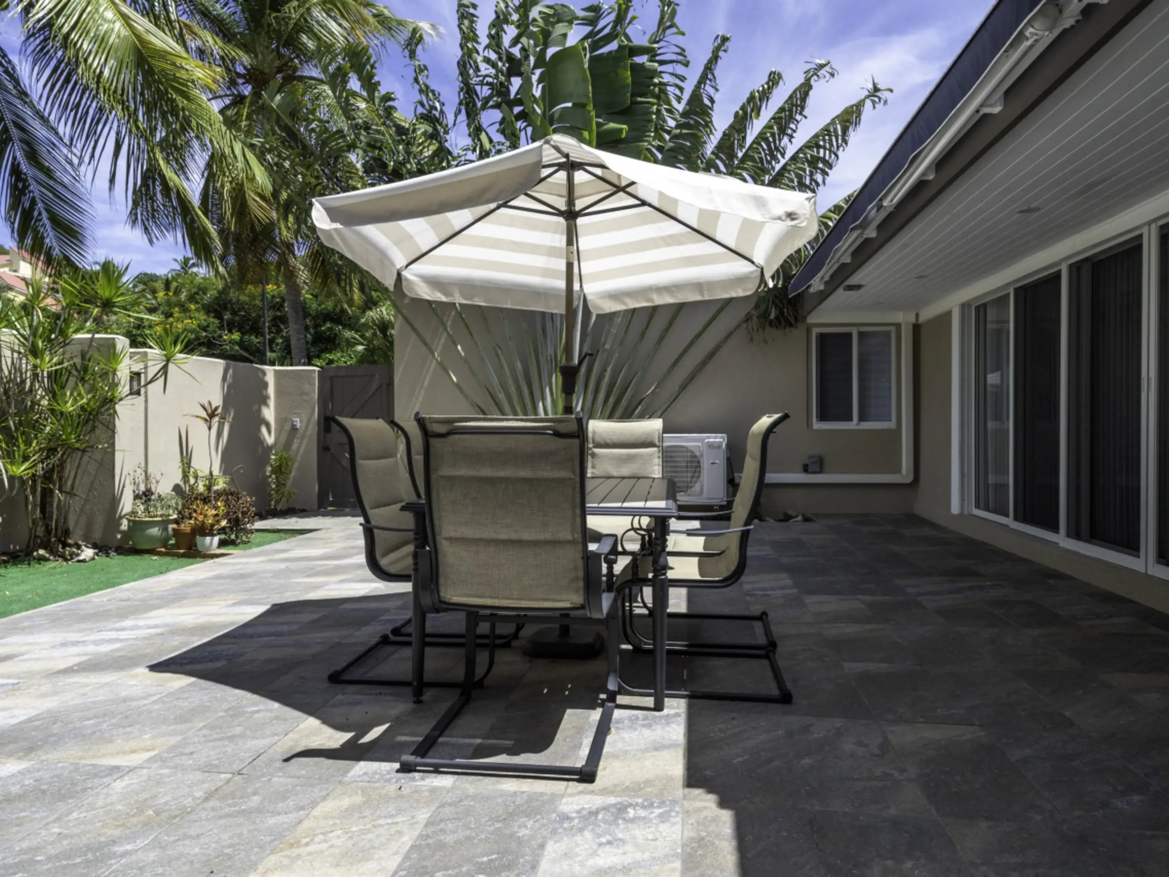Outdoor patio with a table, chairs, and an umbrella, surrounded by palm trees.