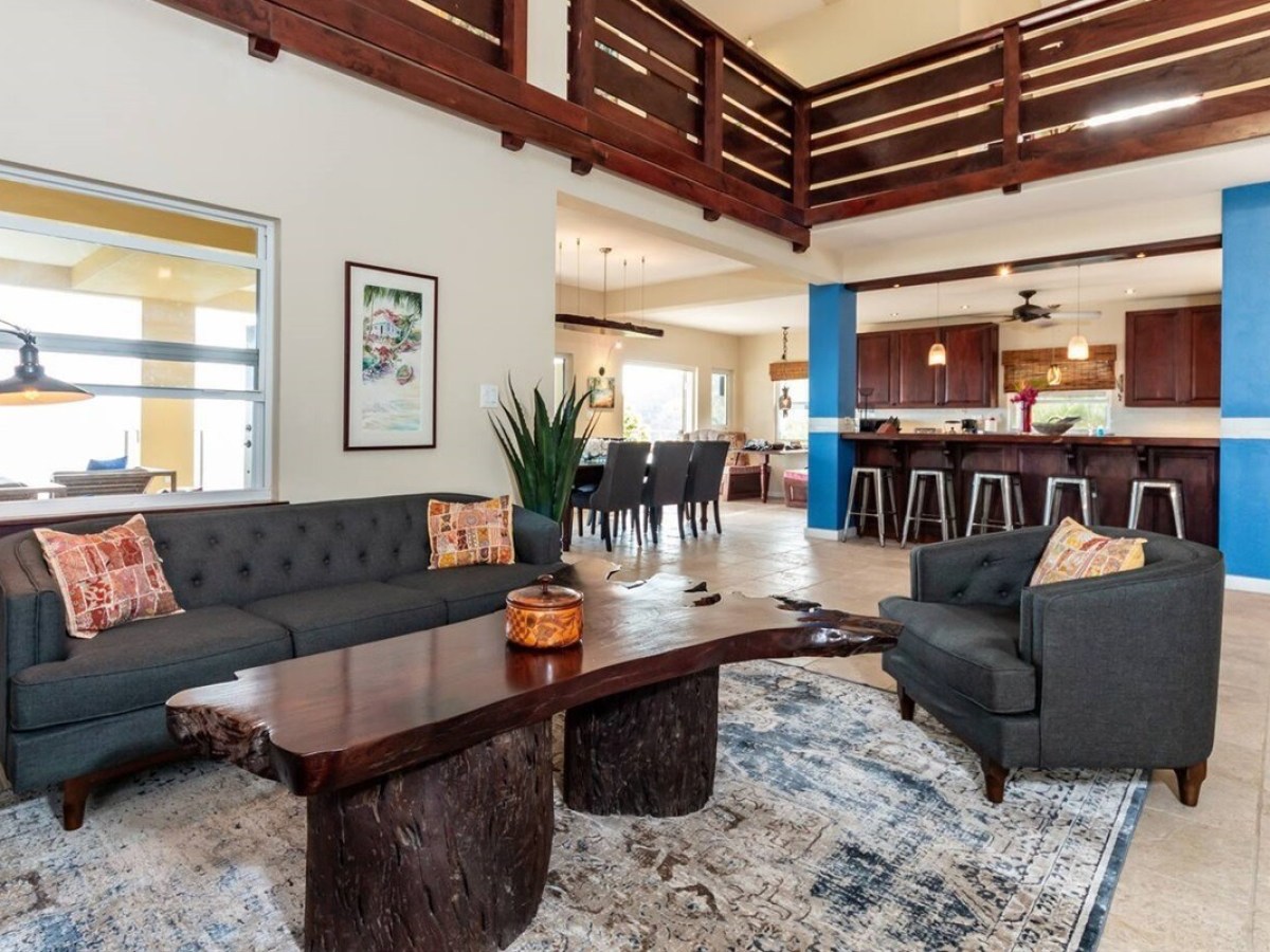Open living room with dark couches, wooden coffee table, and kitchen bar in the background.