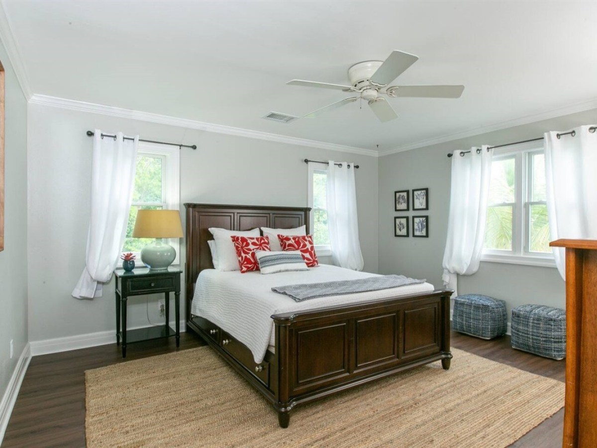 Bedroom with a dark wooden bed, white bedding, red pillows, and light curtains.